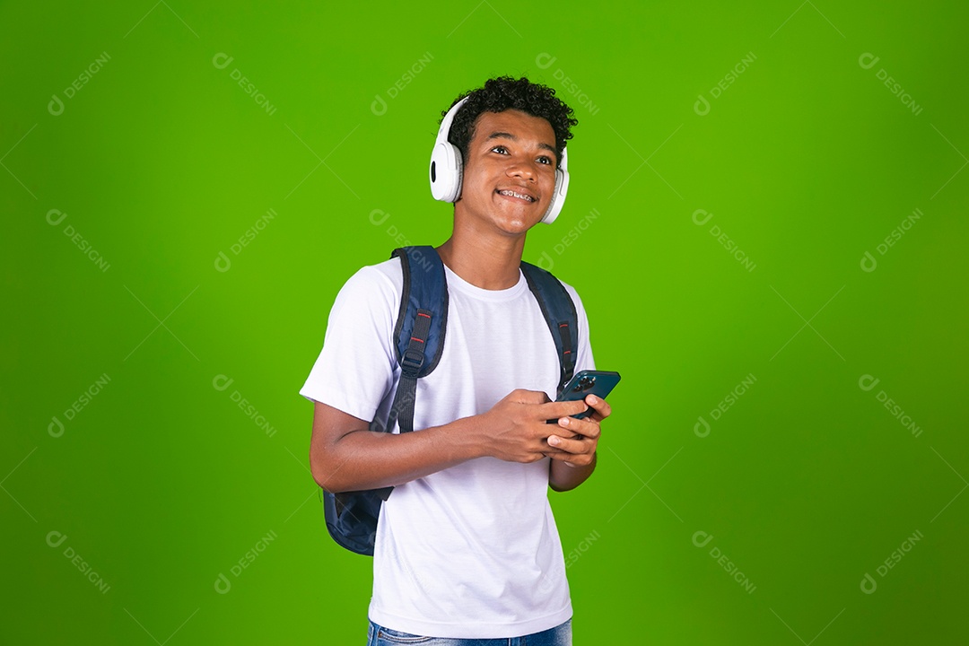 Lindo garoto negro usando fone de ouvido e mochila e segurando smartfhone sobre fundo verde isolado