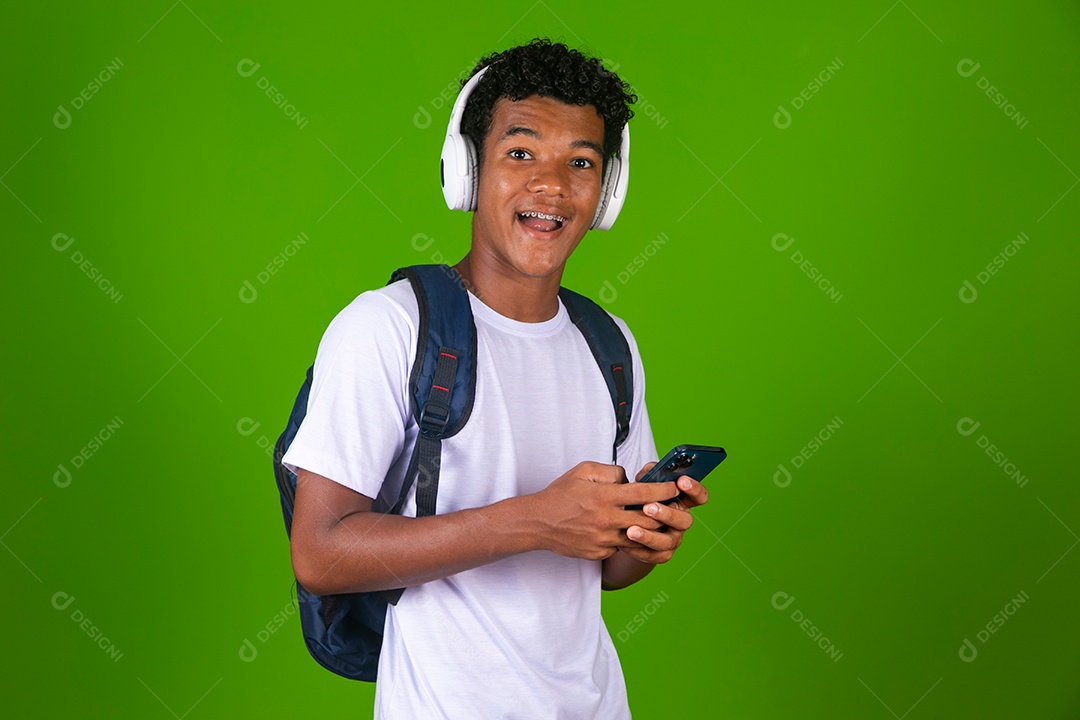 Lindo garoto negro usando fone de ouvido e mochila e segurando smartfhone sobre fundo verde isolado