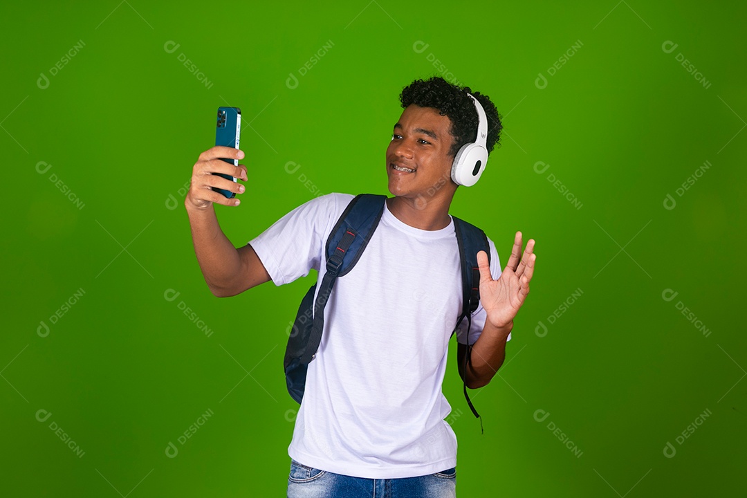 Lindo garoto negro usando fone de ouvido e mochila e segurando smartfhone sobre fundo verde isolado