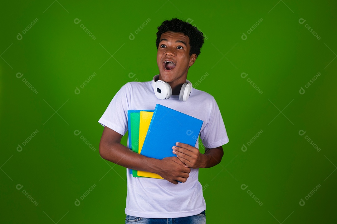 Lindo garoto negro sorridente com fone de ouvido segurando cadernos sobre fundo verde isolado