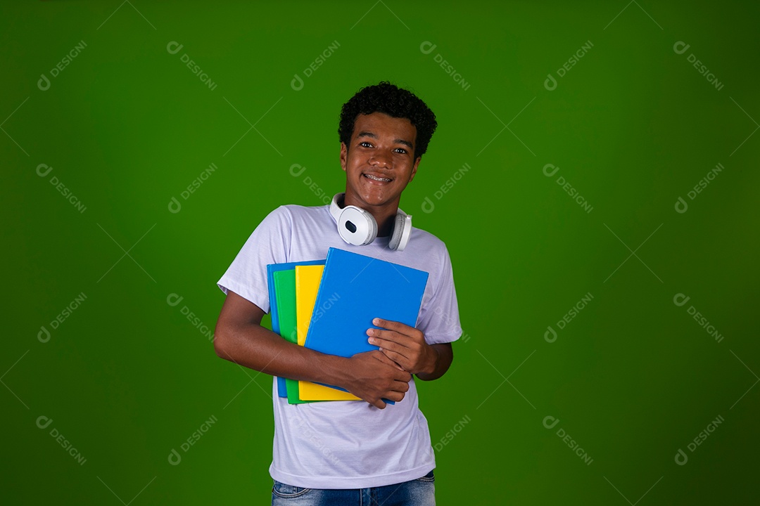Lindo garoto negro sorridente com fone de ouvido segurando cadernos sobre fundo verde isolado