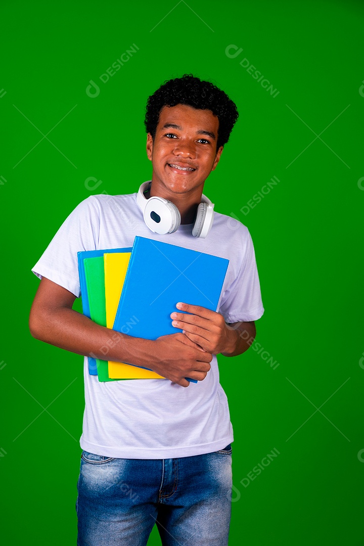 Lindo garoto negro sorridente com fone de ouvido segurando cadernos sobre fundo verde isolado