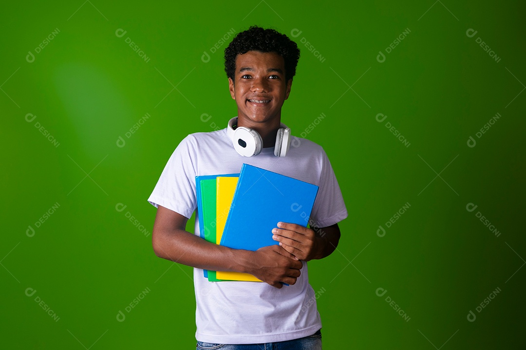 Lindo garoto negro sorridente com fone de ouvido segurando cadernos sobre fundo verde isolado