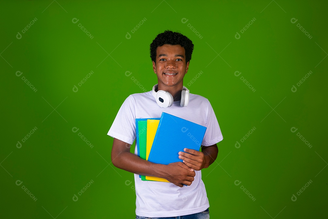Lindo garoto negro sorridente com fone de ouvido segurando cadernos sobre fundo verde isolado