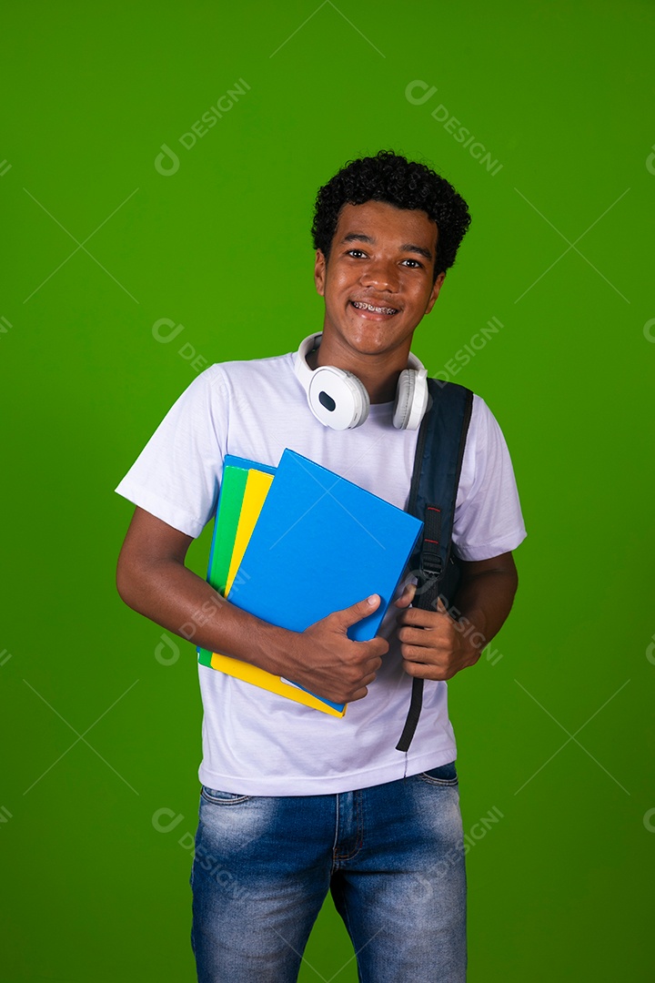 Lindo garoto negro usando bolsa e fone de ouvido segurando caderno sobre fundo verde isolado