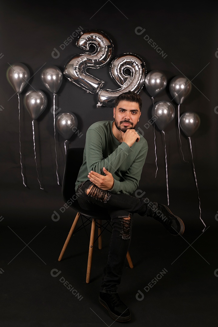Lindo homem sentado fazendo aniversário sobre fundo com balões isolado