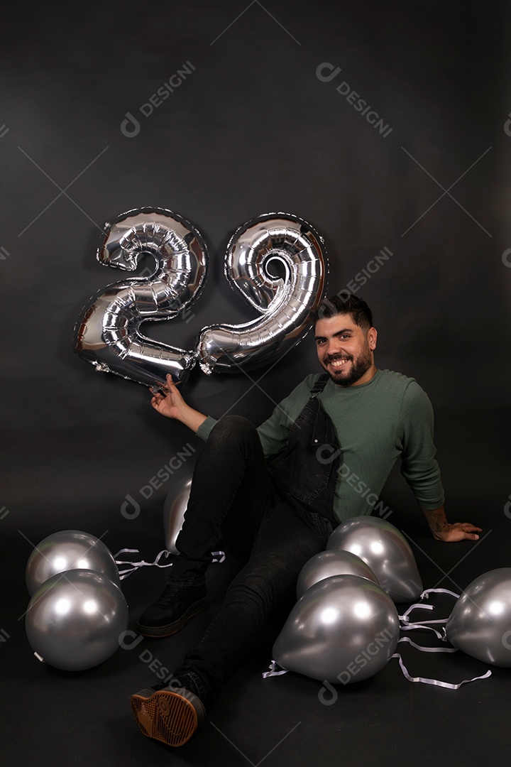 Linda homem sorridente com macacão preto segurando balões sobre fundo isolado