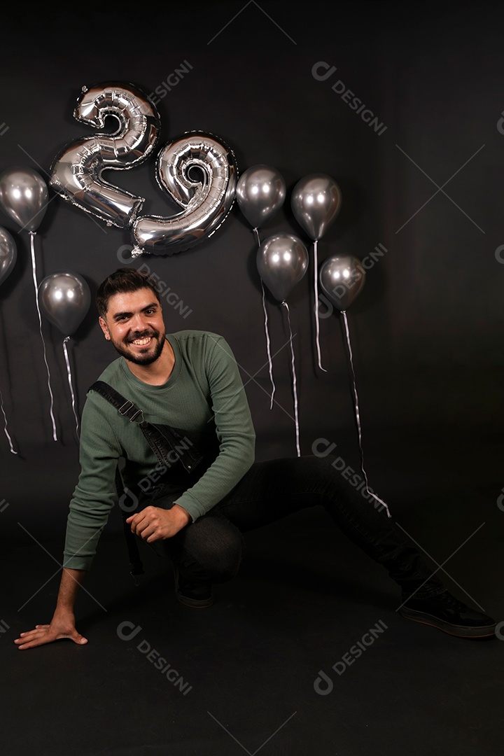 Lindo homem sorridene usando macacão preto sobre fundo com balões isolado