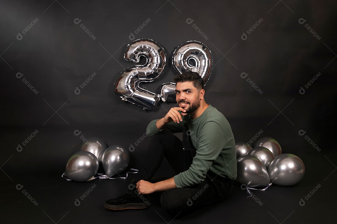 Lindo homem sorridente sentado fazendo aniversário sobre fundo com balões isolado