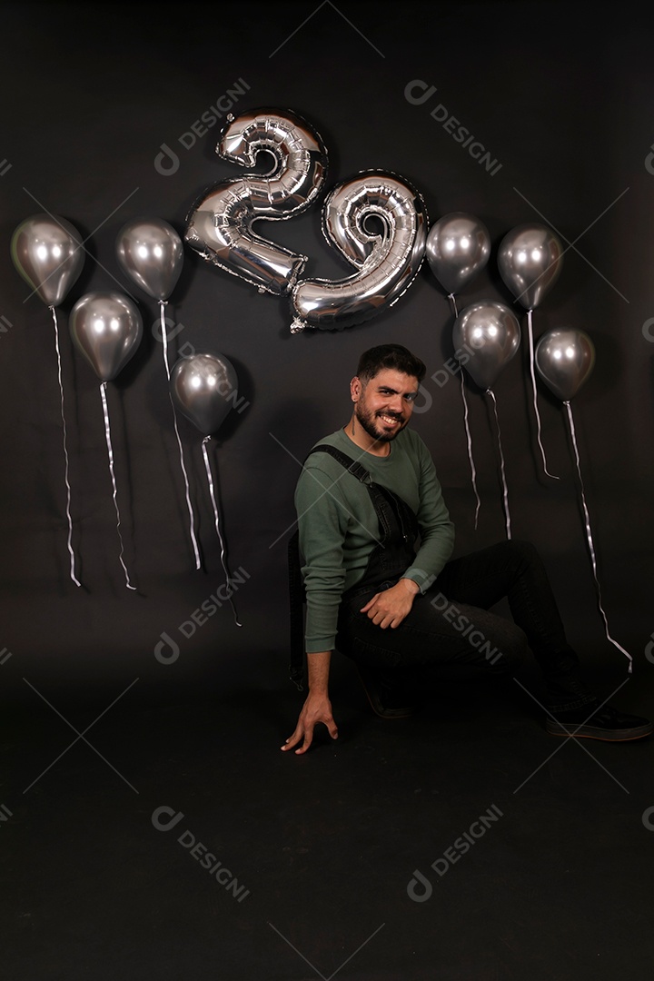 Lindo homem sorridente sentado fazendo aniversário sobre fundo com balões isolado
