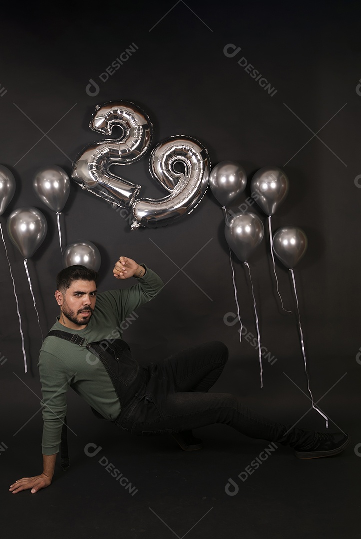 Lindo homem sentado fazendo aniversário sobre fundo com balões isolado