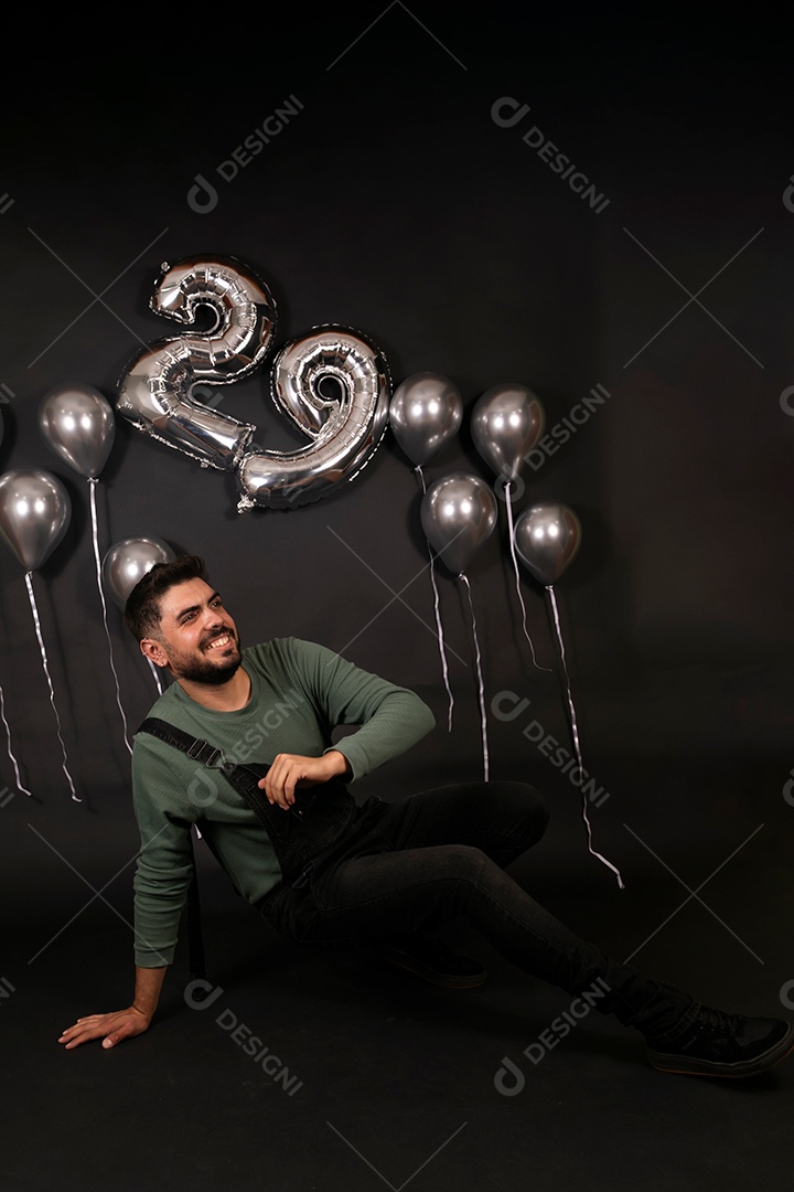 Lindo homem sorridente sentado fazendo aniversário sobre fundo com balões isolado