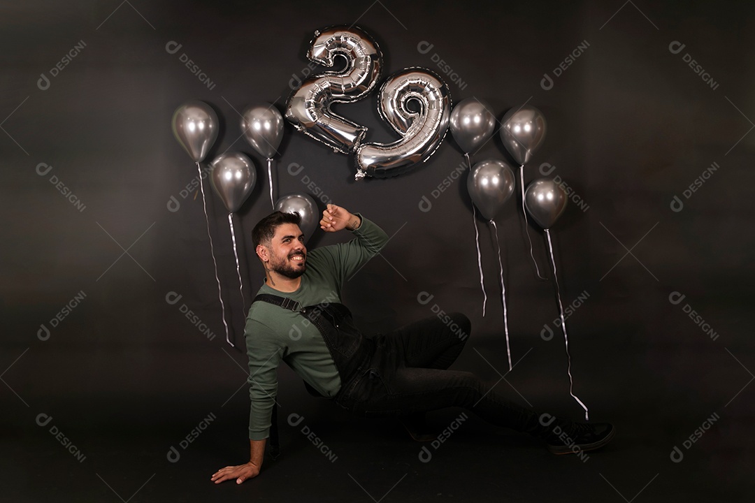 Lindo homem sorridente sentado fazendo aniversário sobre fundo com balões isolado