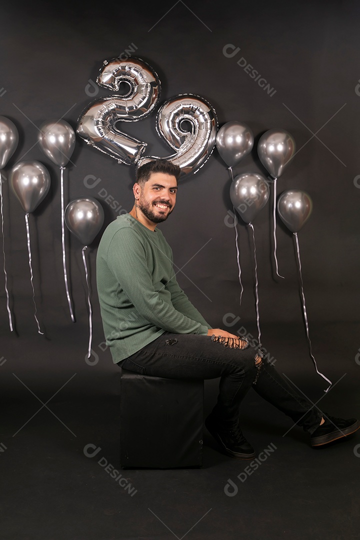 Lindo homem sorridente sentado fazendo aniversário sobre fundo com balões isolado