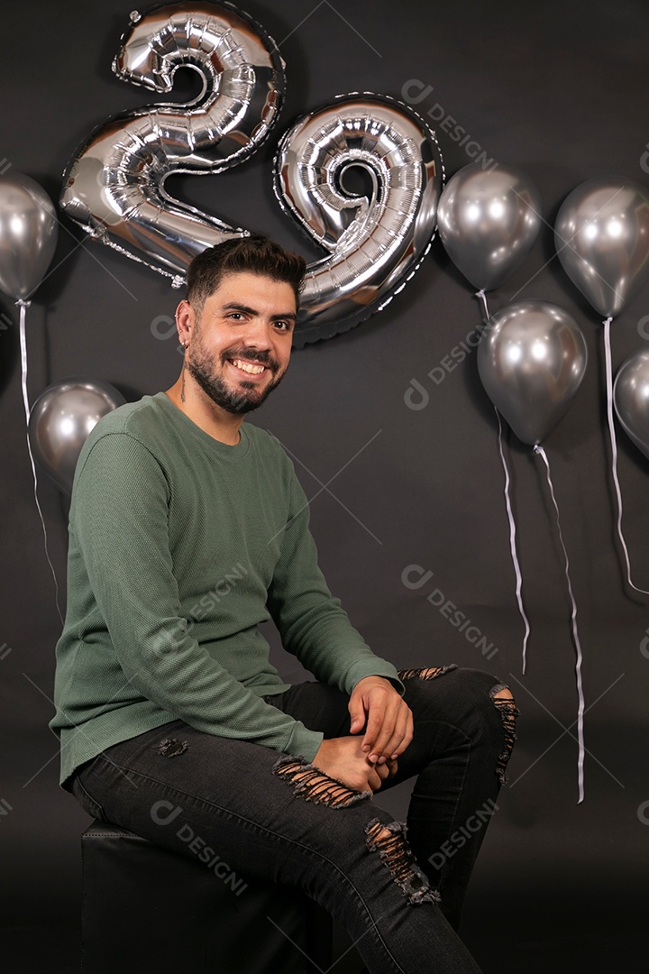 Lindo homem sorridente sentado fazendo aniversário sobre fundo com balões isolado