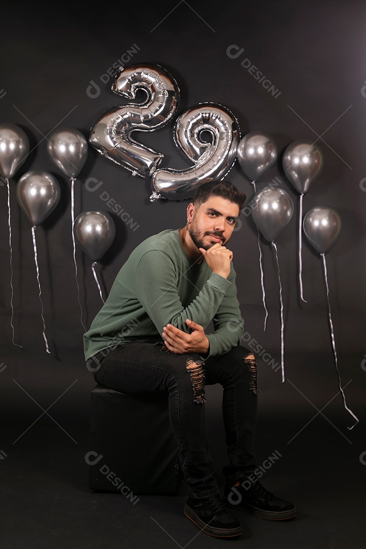 Lindo homem sentado fazendo aniversário sobre fundo com balões isolado