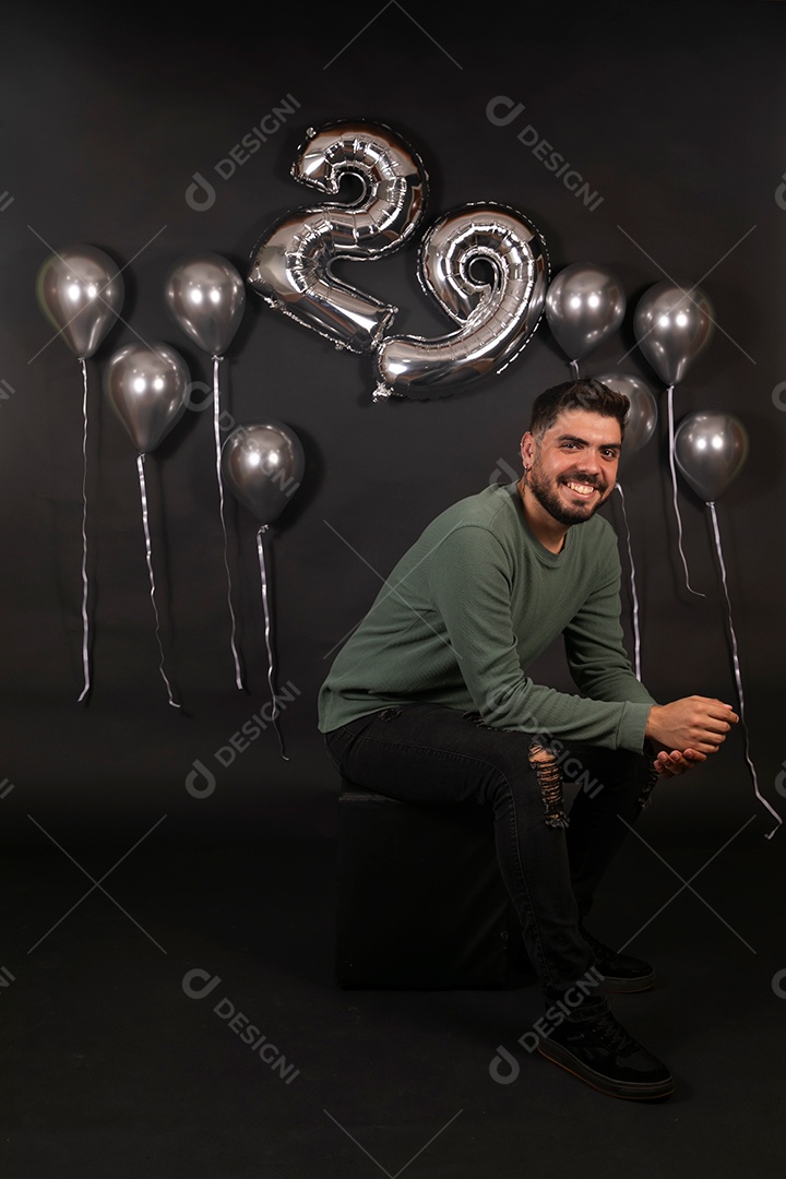 Lindo homem sorridente sentado fazendo aniversário sobre fundo com balões isolado