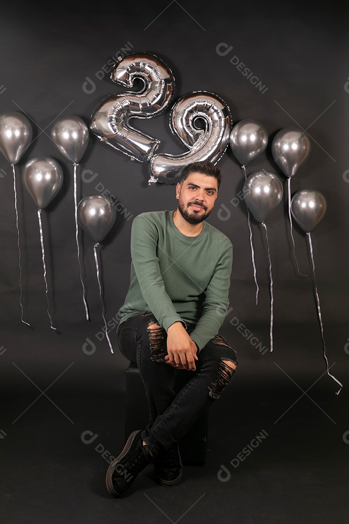 Lindo homem sentado fazendo aniversário sobre fundo com balões isolado