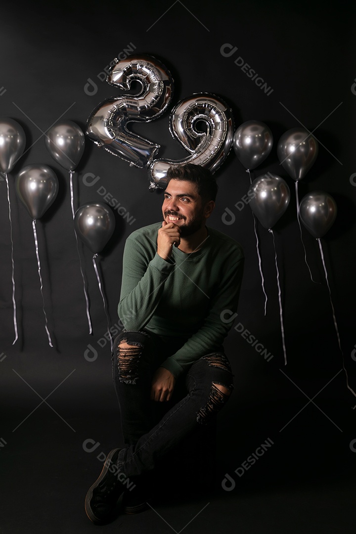 Lindo homem sorridente sentado fazendo aniversário sobre fundo com balões isolado