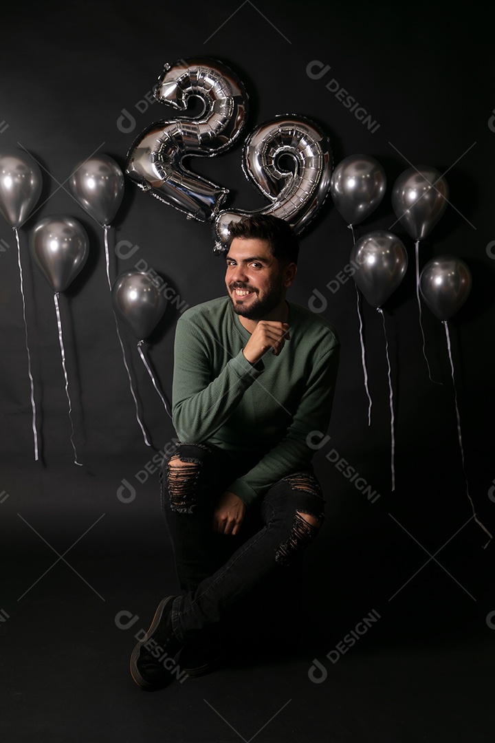 Lindo homem sorridente sentado fazendo aniversário sobre fundo com balões isolado