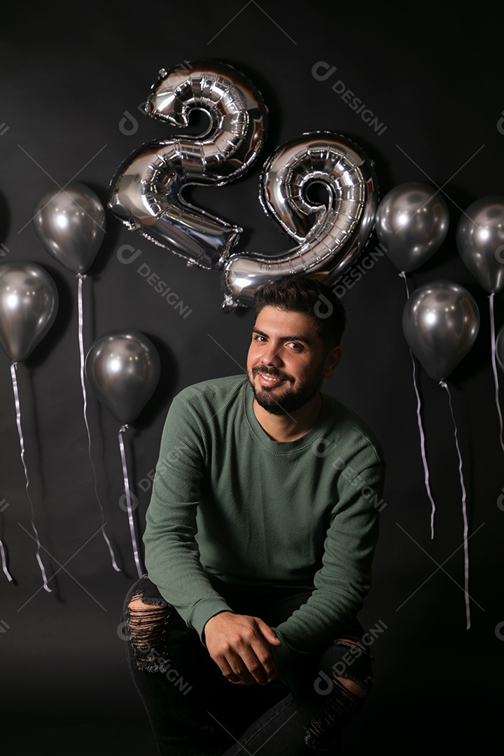 Lindo homem sorridente sentado fazendo aniversário sobre fundo com balões isolado