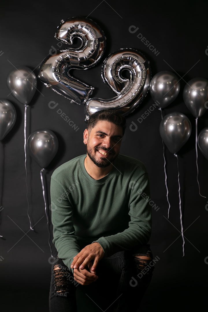 Lindo homem sorridente sentado fazendo aniversário sobre fundo com balões isolado