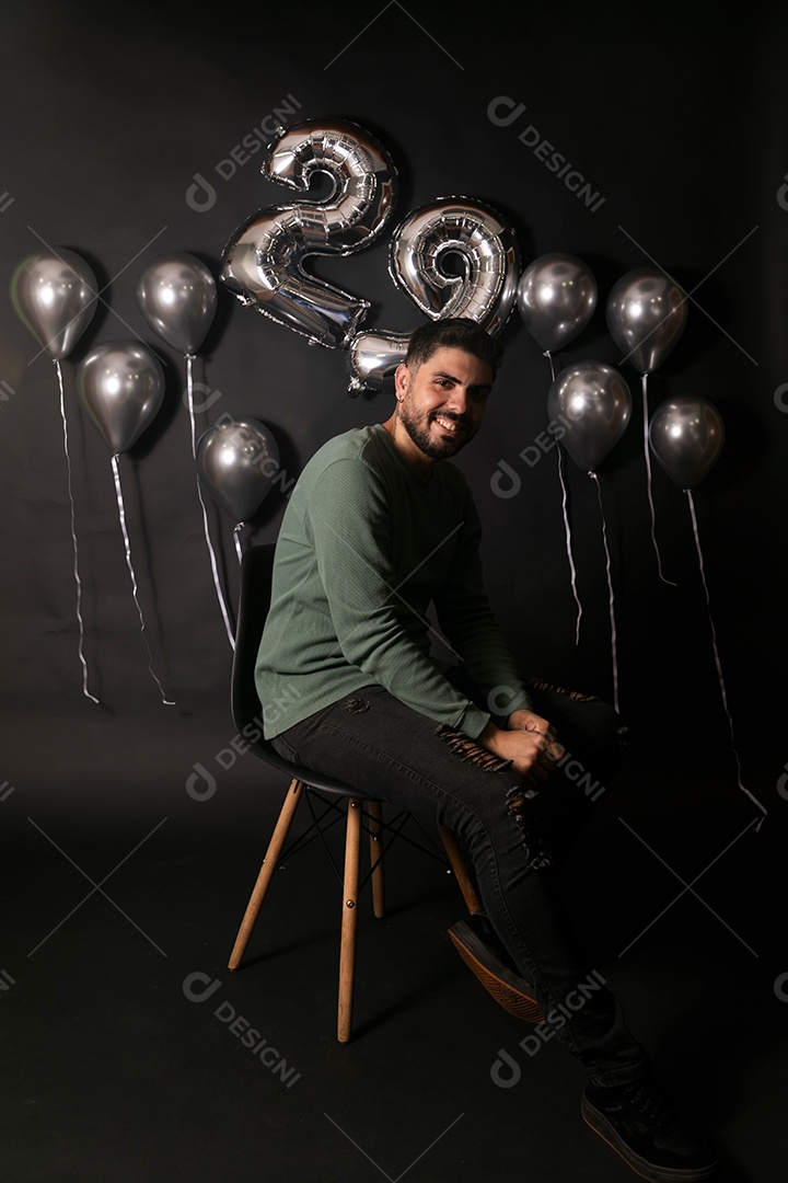 Lindo homem sorridente sentado fazendo aniversário sobre fundo com balões isolado