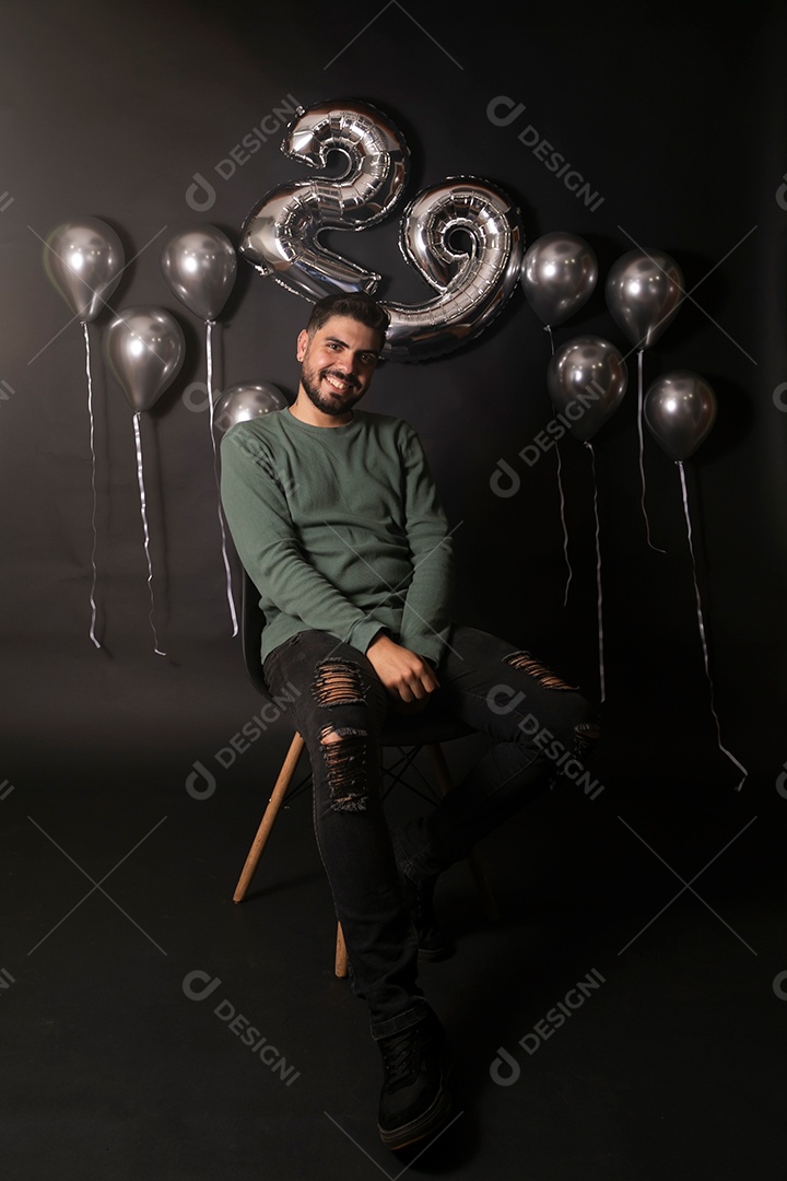 Lindo homem sorridente sentado fazendo aniversário sobre fundo com balões isolado
