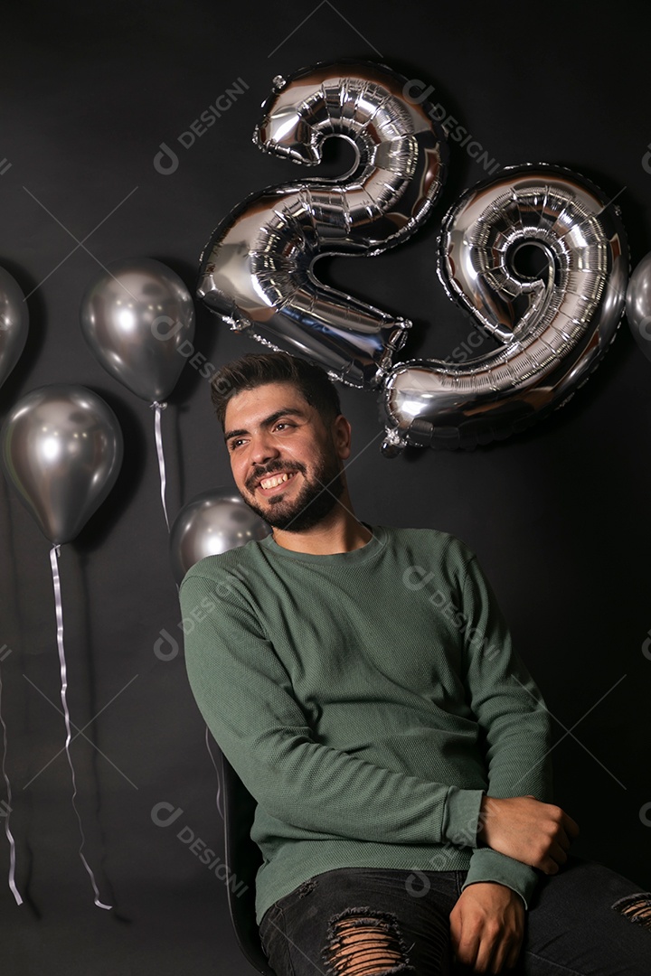 Lindo homem sorridente sentado fazendo aniversário sobre fundo com balões isolado