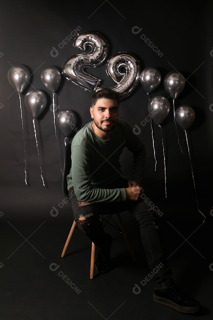 Lindo homem sentado fazendo aniversário sobre fundo com balões isolado