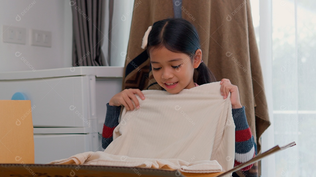 Linda garotinha usando roupa de tricor colorida segurando suéter branco sobre fundo de um quarto isolado