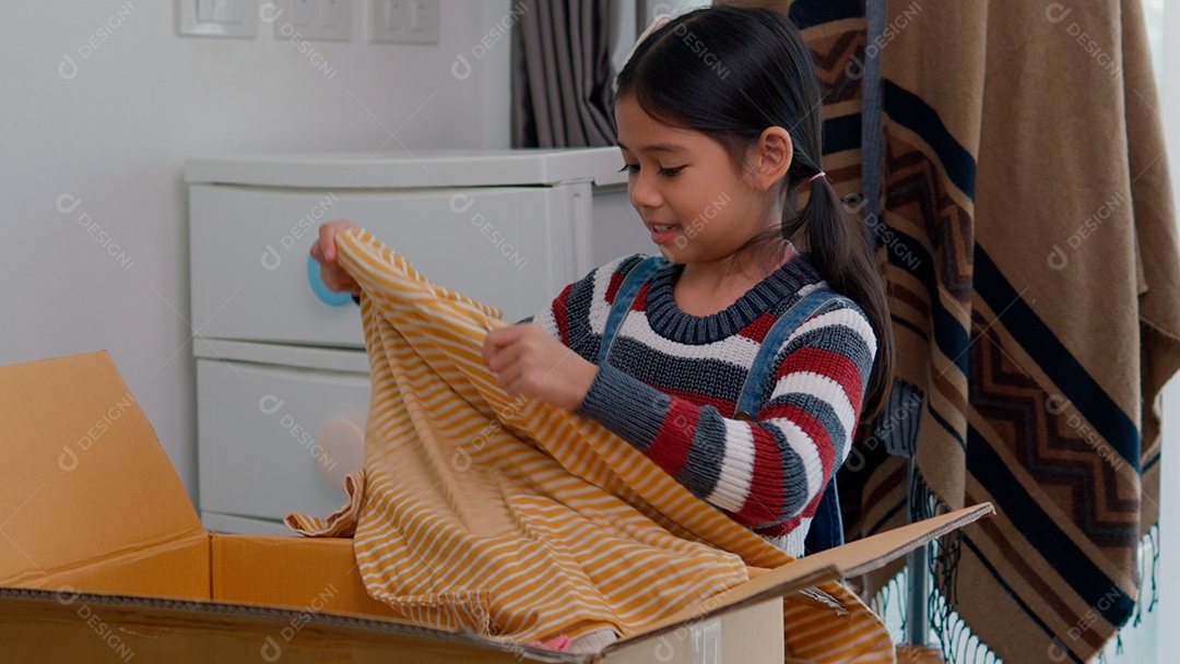 Linda garotinha usando roupa de tricor colorida segurando suéter sobre fundo de um quarto isolado