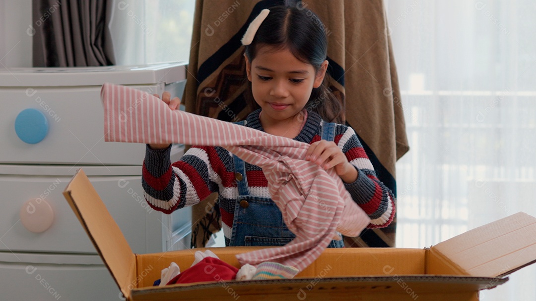 Linda garotinha usando roupa de tricor colorida segurando suéter sobre fundo de um quarto isolado