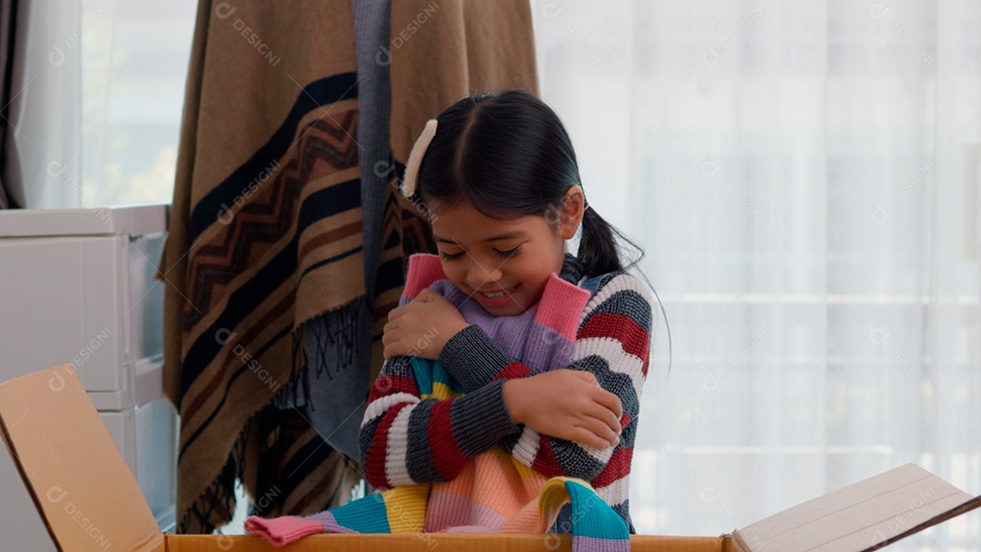 Linda garotinha usando roupa de tricor colorida segurando suéters sobre fundo de um quarto isolado