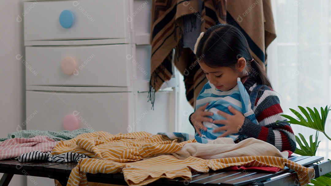 Linda garotinha usando roupa de tricor colorida segurando suéter sobre fundo de um quarto isolado