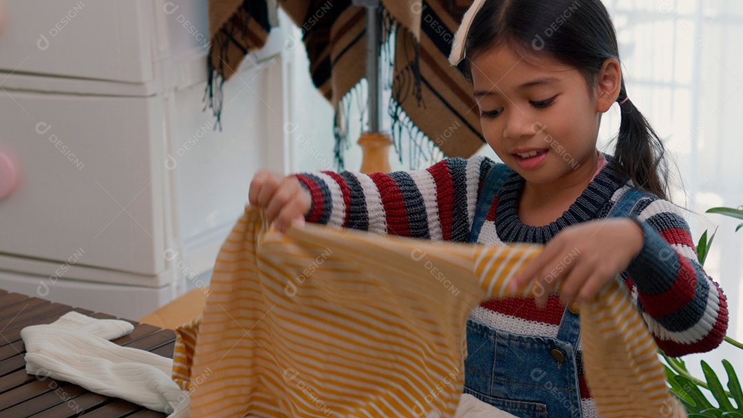 Linda garotinha usando roupa de tricor colorida segurando suéter sobre fundo de um quarto isolado
