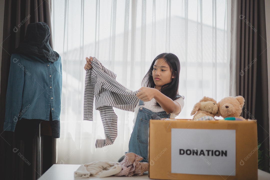 Linda garota sorridente segurando roupas e brinquedos para doação