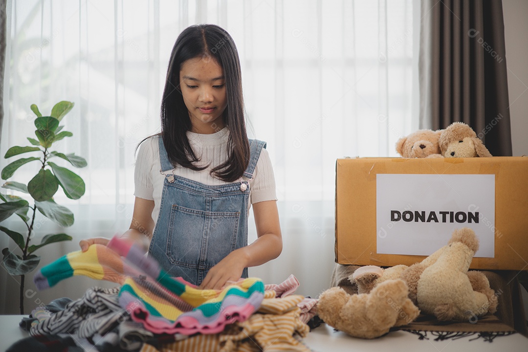 Linda garota sorridente segurando roupas e brinquedos para doação