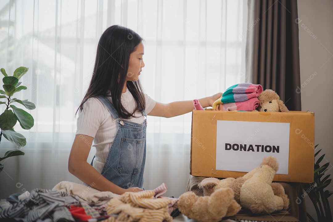Linda garota sorridente segurando roupas e brinquedos para doação