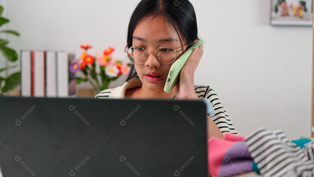 Linda mulher de óculos em chamada em smartphone e mechendo em leptop sobre fundo de um vestiário