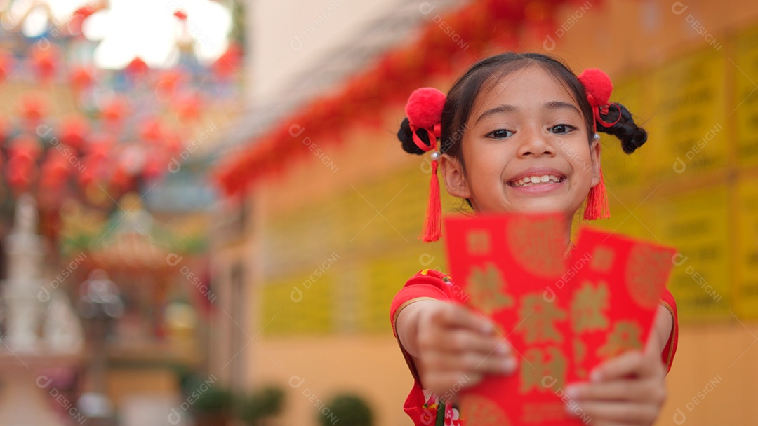 Linda menina asiática feliz vestindo uma decoração de cheongsam tradicional chinesa vermelha segurando envelopes vermelhos nas mãos sobre fundo desfocado