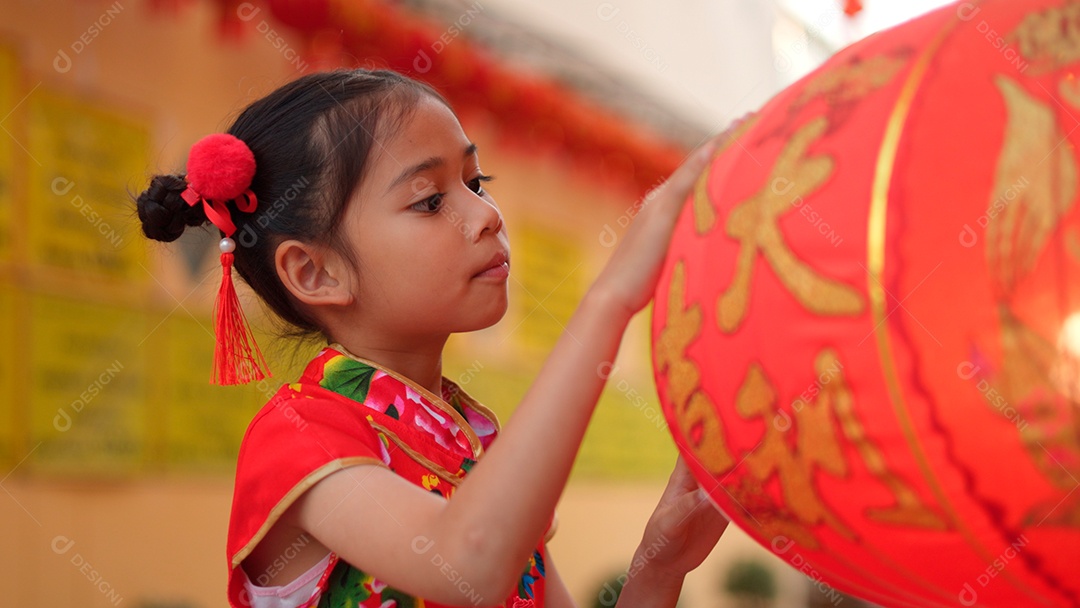 Linda menina asiática feliz vestindo uma decoração de cheongsam tradicional chinesa vermelha com mãos tocando em lâmpadas chinesa sobre fundo desfocado