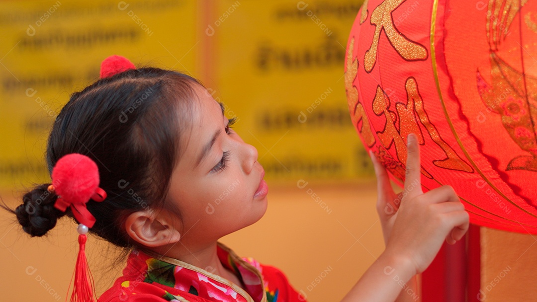 Linda menina asiática feliz vestindo uma decoração de cheongsam tradicional chinesa vermelha com mãos tocando em lâmpadas chinesa sobre fundo desfocado