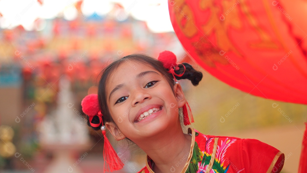 Linda menina asiática feliz vestindo uma decoração de cheongsam tradicional chinesa vermelha com mãos tocando em lâmpadas chinesa sobre fundo desfocado
