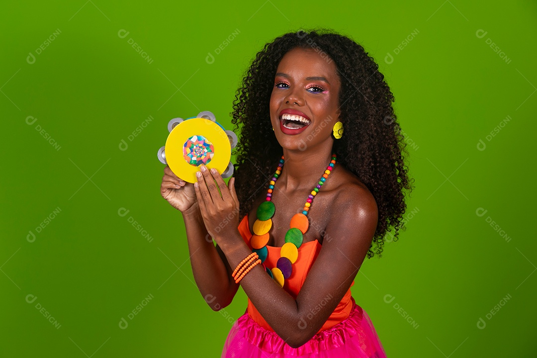 Linda morena do cabelo cacheado sorridente fantasiada segurando pandeiro sobre fundo verde isolado