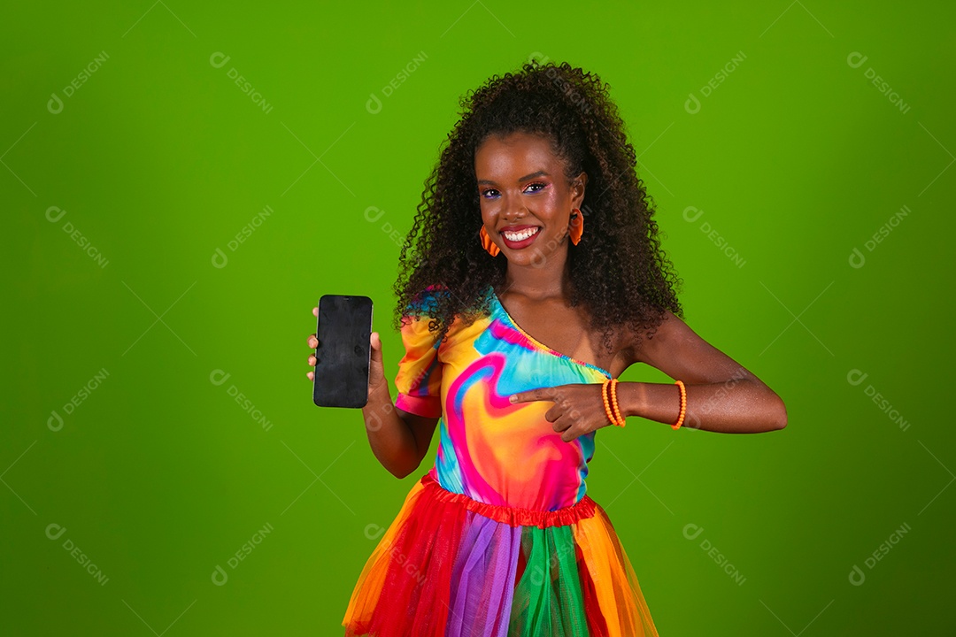 Linda morena do cabelo cacheado sorridente usando conjunto de carnaval segurando smartfhone sobre fundo verde isolado