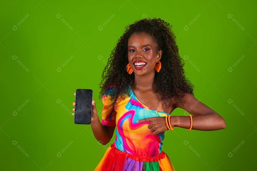 Linda morena do cabelo cacheado sorridente usando conjunto de carnaval segurando smartfhone sobre fundo verde isolado