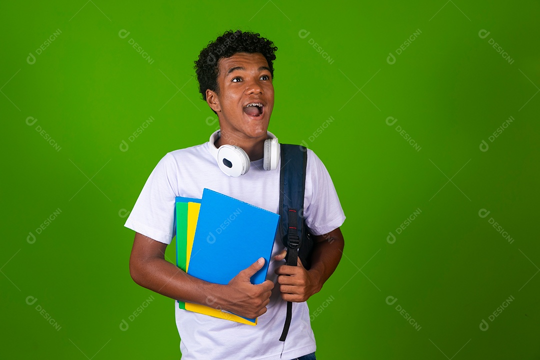 Lindo garoto negro de camisa branca usando bolsa e fone de ouvido segurando caderno escolares sobre fundo verde isolado