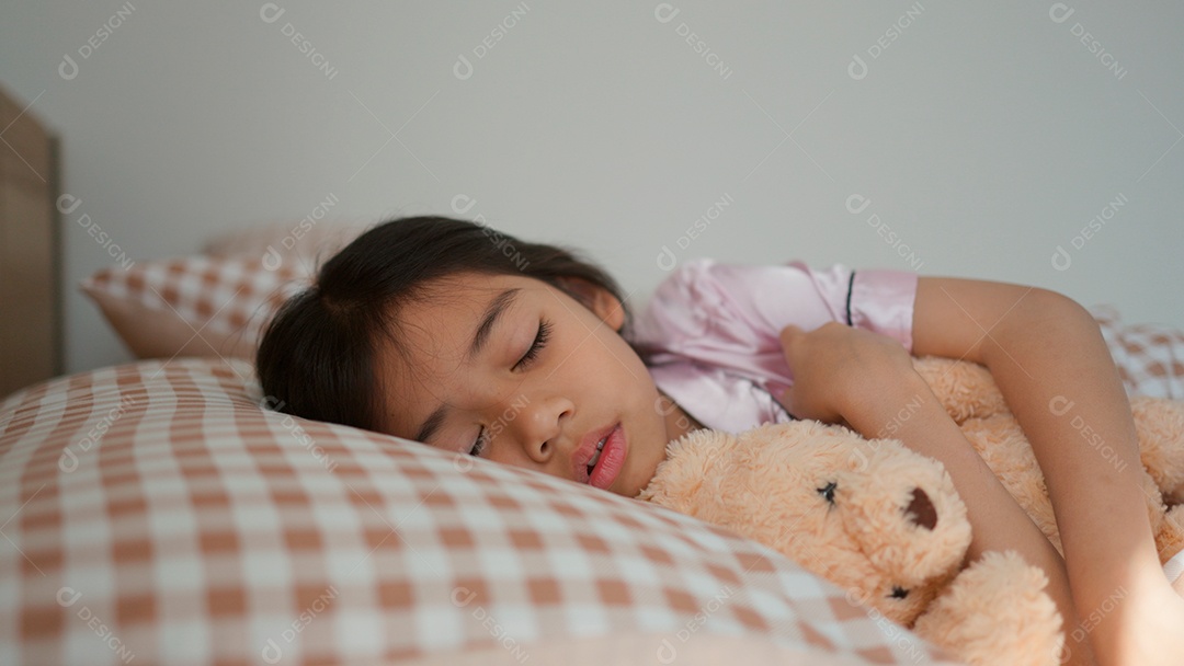 Linda menina dormindo sobre sua cama abraçando seu ursinho de pelúcia