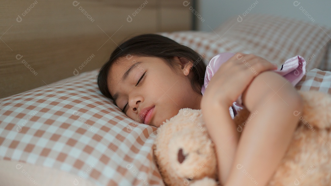 Linda menina dormindo sobre sua cama abraçando seu ursinho de pelúcia